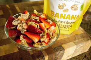 A bowl of banana coated walnut snacks with sliced strawberries