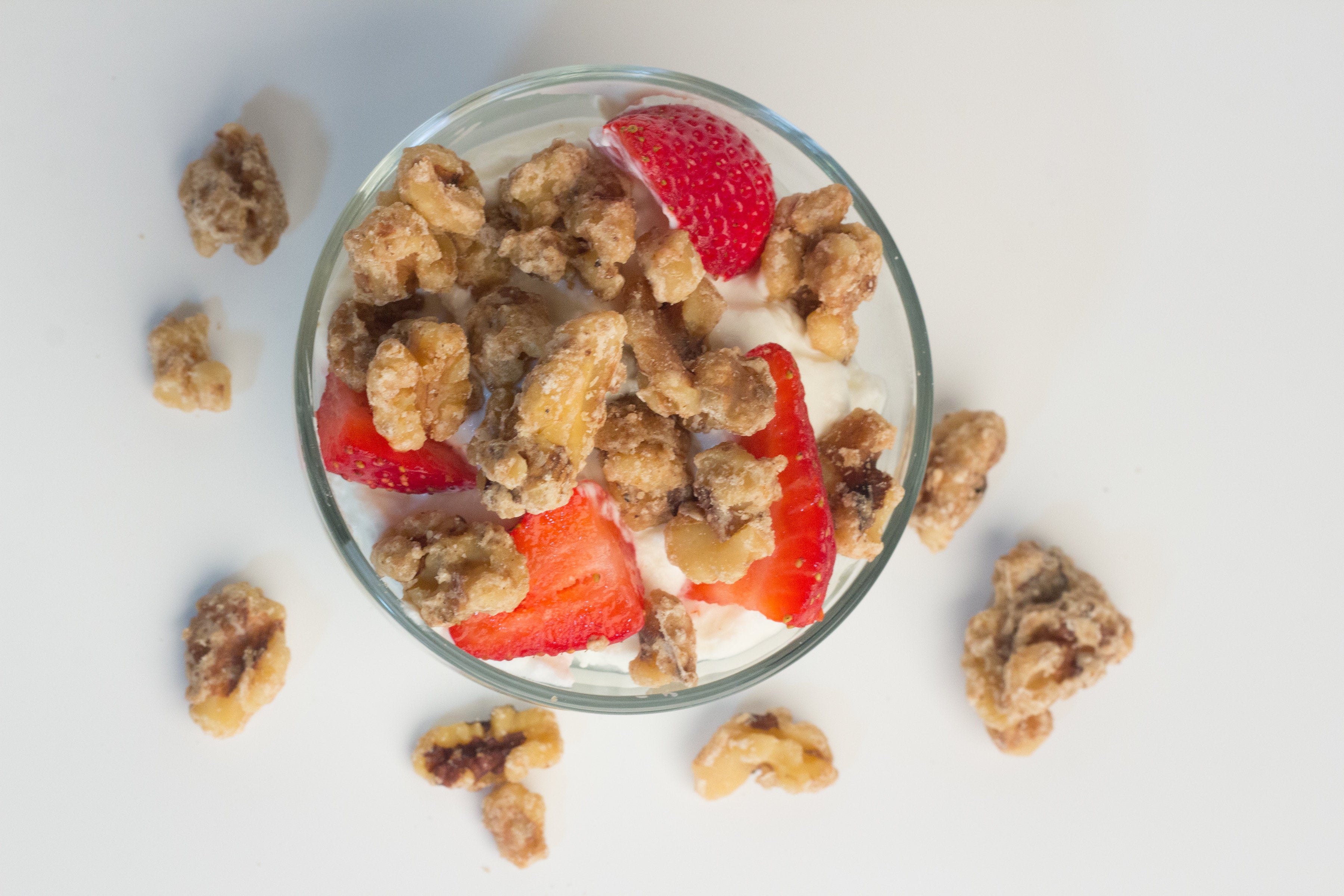 An aerial view of a bowl of yogurt topped with banana walnut snacks and strawberries