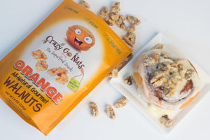 A bag of orange coated walnut snacks spilled and a cinnamon roll topped with orange coated walnut snacks