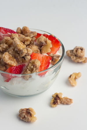 A bowl of yogurt with strawberries and orange coated walnut snacks as toppings