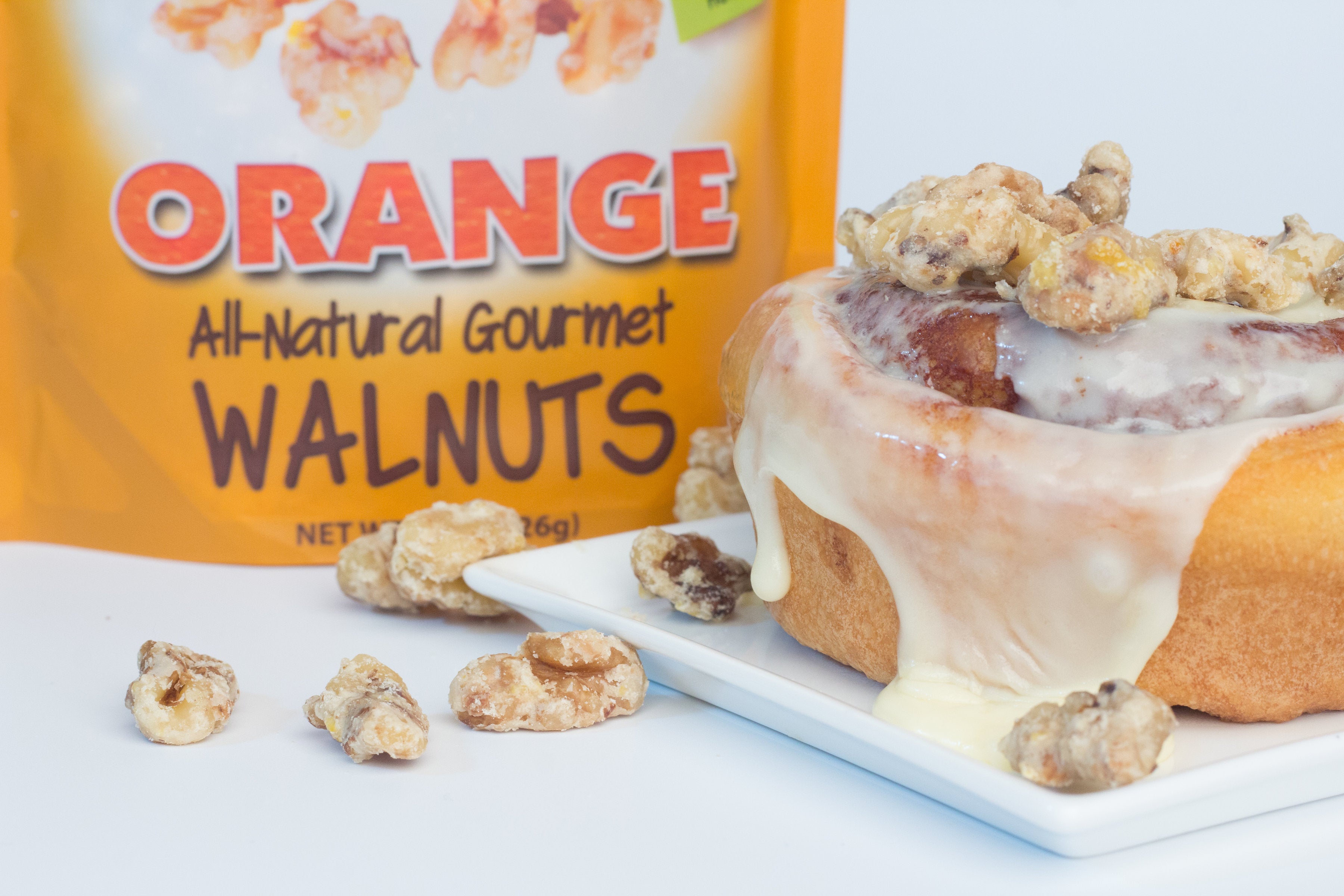 Orange coated walnut snacks being used as a topping for a cinnamon roll.
