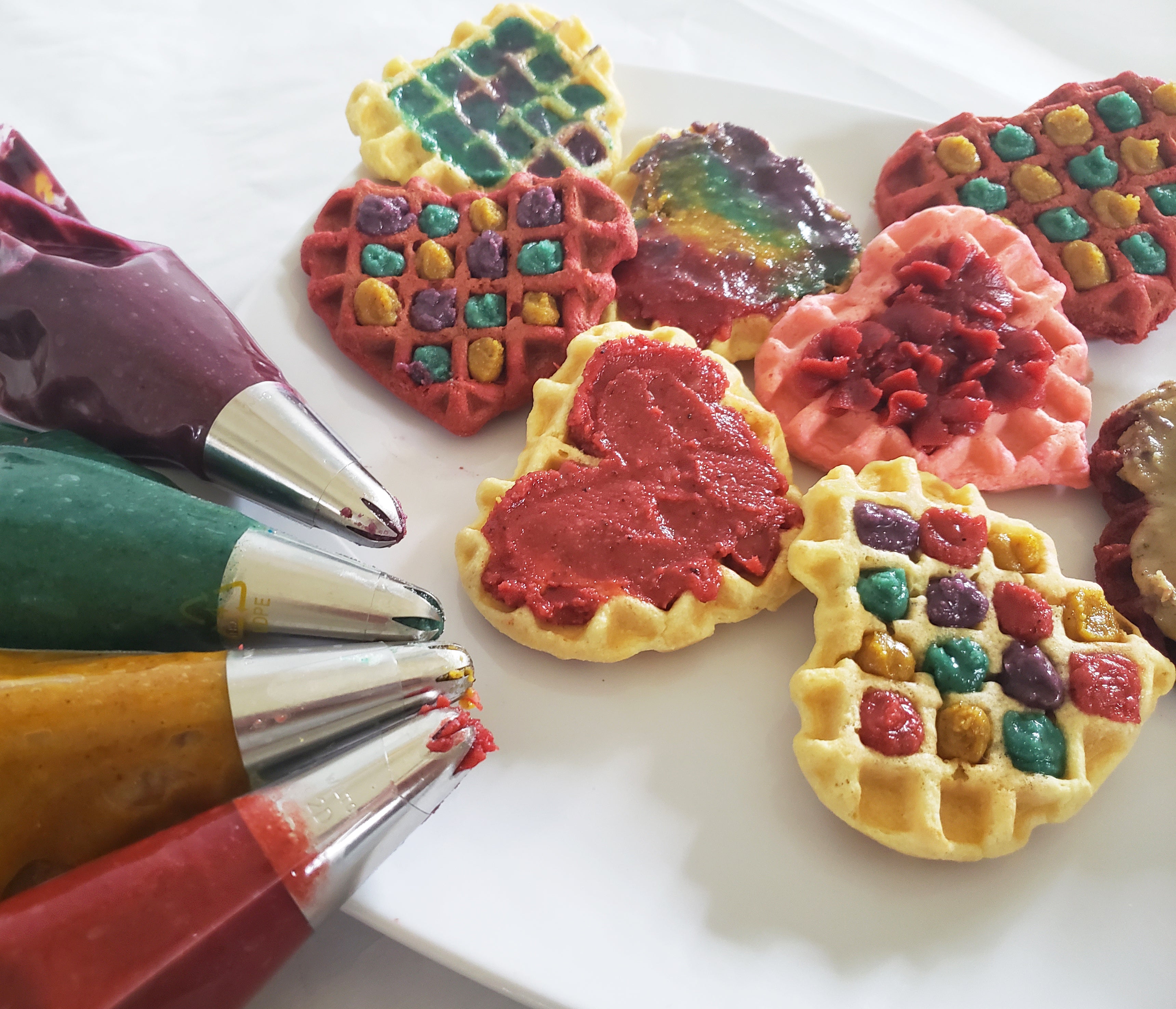 Heart shaped waffles with fun colored walnut butter in pastry bags