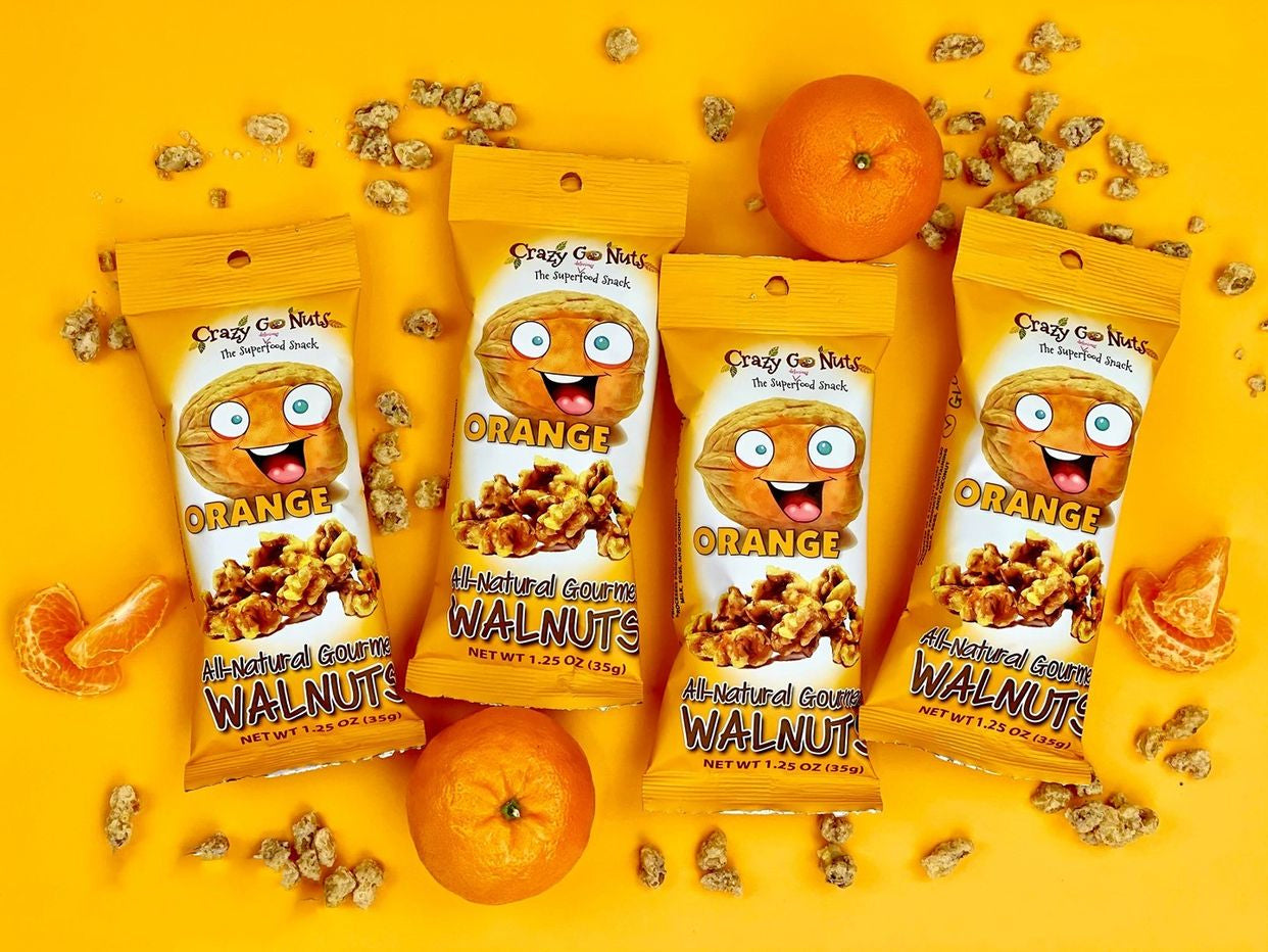 Bags of orange coated walnut snacks strewn about among whole oranges